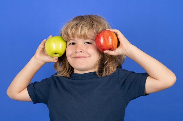 Enfant garçon choisissant entre une pomme rouge et une pomme verte isolée sur fond bleu