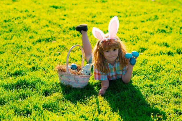 Enfant garçon en costume de lapin avec des oreilles de lapin chassant les oeufs de pâques dans le parc vacances de printemps