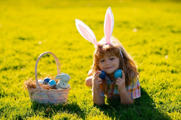Enfant garçon en costume de lapin avec des oreilles de lapin chassant les oeufs de pâques dans le parc