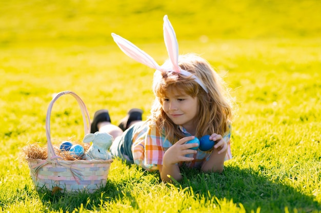 Enfant garçon en costume de lapin avec des oreilles de lapin chassant les oeufs de pâques portant sur l'herbe dans le parc