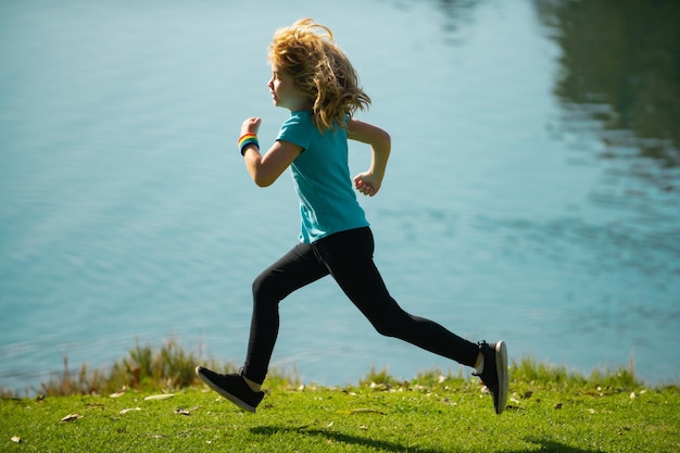 Enfant garçon courant ou faisant du jogging près du lac sur l'herbe dans le parc Petits coureurs faisant du jogging à l'extérieur dans la nature estivale Enfant sportif faisant du jogging dans un parc Sports de plein air et fitness pour les enfants