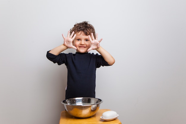 Enfant, un garçon dans un T-shirt noir se lave les mains avec du savon sur un mur blanc