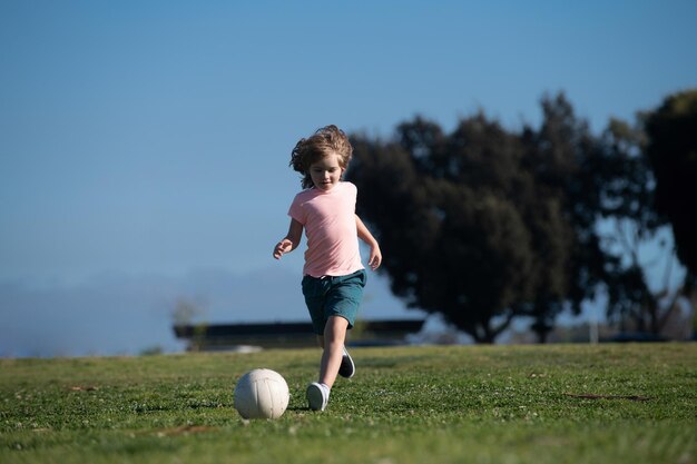 Enfant garçon donnant un coup de pied au football sur le terrain de sport pendant un match de football