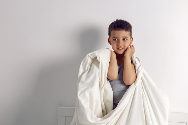 L'enfant garçon est fou de s'amuser dans un lit blanc dans la chambre des enfants avec une couverture