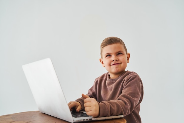 Enfant garçon étudie en ligne avec un ordinateur portable et des sourires Éducation en ligne et apprentissage en ligne Enfant prenant des cours en ligne sur un ordinateur portable