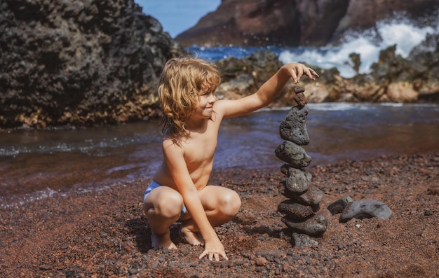 Enfant garçon faisant une pile de galets en pierre sur fond de mer pour la méditation de l'équilibre du spa et le thème zen