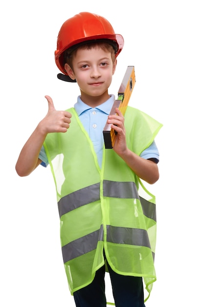 Enfant garçon avec gilet de niveau de construction et casque isolé sur blanc montre le pouce vers le haut de geste, futur travailleur de la construction