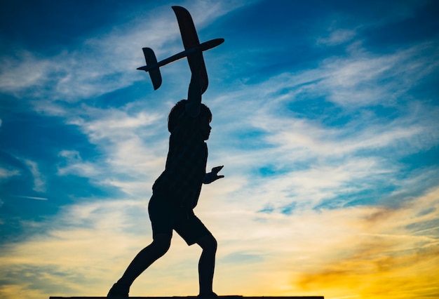 Enfant garçon jouant avec un avion jouet pendant le coucher du soleil souvenirs d'enfance beau ciel au-dessus de l'enfant de la prairie