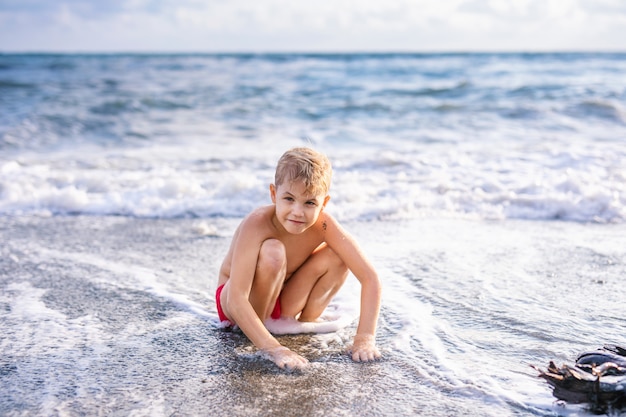 Enfant Garçon Jouant Dans Les Vagues Sur La Plage Au Coucher Du Soleil De L'été, Enfant Regardant Les Vagues Et S'amuser