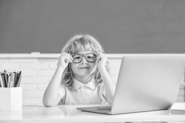 Enfant garçon à lunettes étudie en ligne dans la classe de l'école avec la journée de la connaissance de l'ordinateur portable