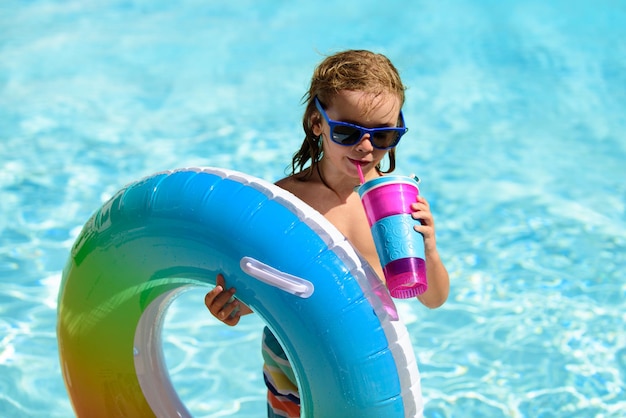 Enfant garçon à lunettes de soleil et cocktail d'été relaxant avec anneau de jouet flottant dans une piscine