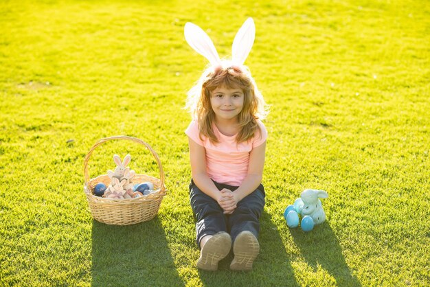 Enfant garçon avec des oeufs de pâques et des oreilles de lapin en plein air enfant mignon ayant joyeuses pâques dans le parc enfants en lapin