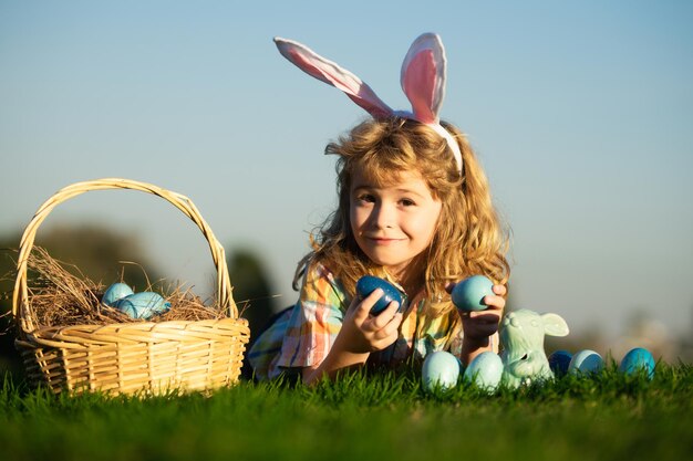 Enfant garçon avec des oeufs de pâques et panier sur l'herbe enfants chassant les oeufs de pâques portant sur l'herbe pâques b...