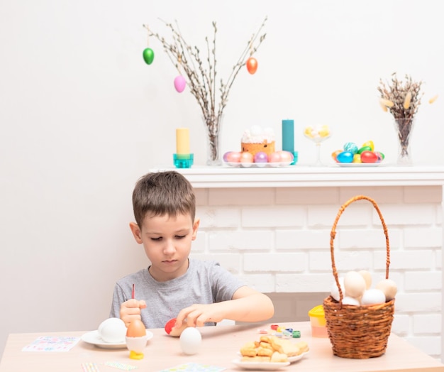Enfant garçon peignant des oeufs de pâques contre une cheminée défocalisée avec des décorations de Pâques dessus Mise au point sélective Joyeuses Pâques concept Processus de fabrication à la maison