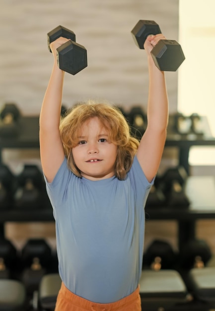 Photo enfant garçon pompant les muscles du biceps avec des haltères enfants de fitness avec deshaltères