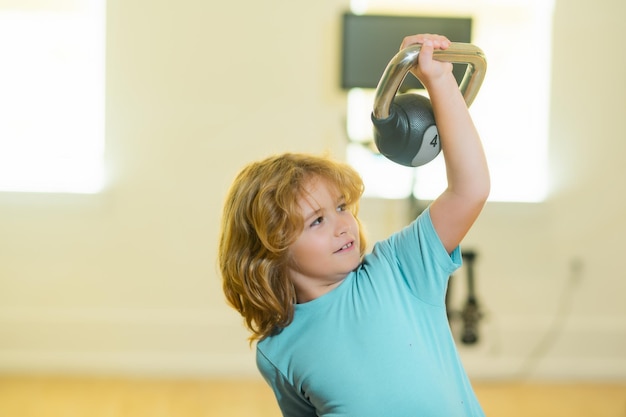 Enfant garçon pompant les muscles du biceps avec kettlebell Fitness enfants avec haltères