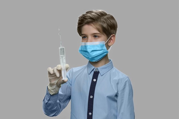 Enfant garçon prépare la seringue pour injection. Enfant de race blanche en masque chirurgical et gants tenant la seringue d'injection. Rêve d'être médecin à l'avenir.