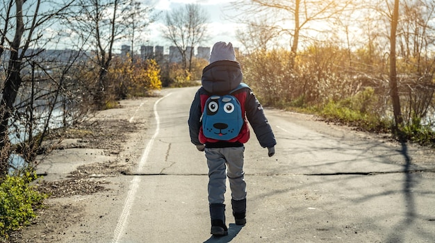 Enfant garçon randonnée avec un sac à dos marche le long de la route à l'extérieur de la ville sur le fond du paysage d'automne