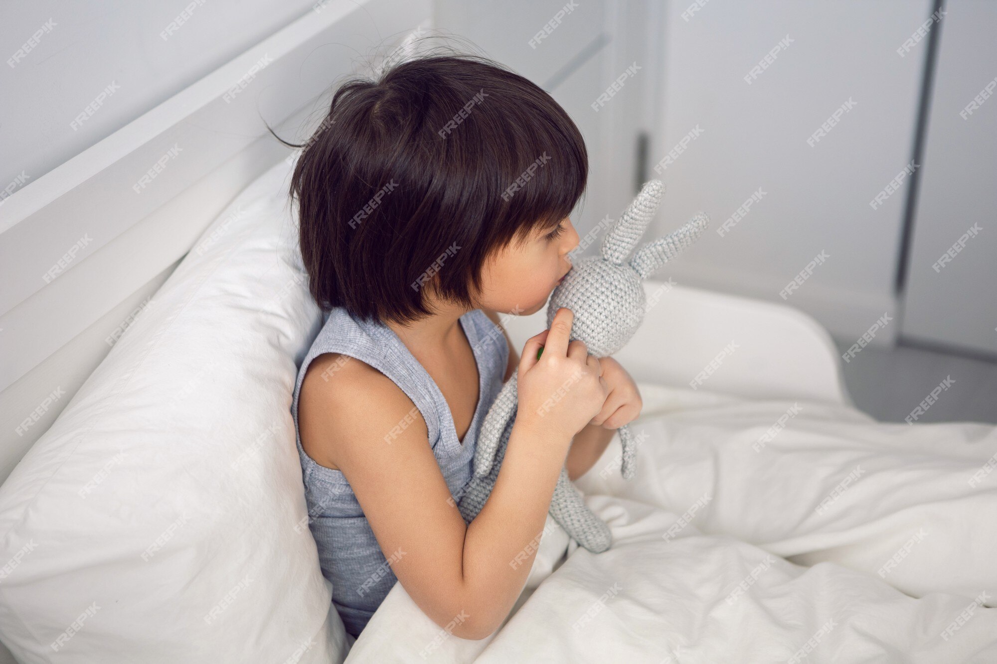 Enfant Garçon Se Trouve Dans Un Lit D'enfant Blanc Avec Une Couverture Dans  Une Chambre Avec Des Lapins Jouets