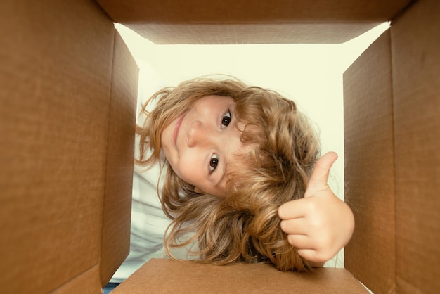 Enfant garçon surpris avec le pouce vers le haut déballant la boîte en carton d'ouverture et regardant à l'intérieur du colis livré