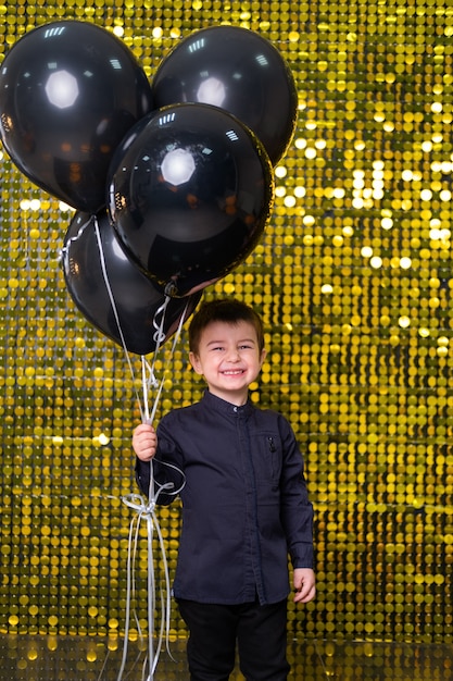 enfant garçon tenant des ballons noirs sur fond avec des paillettes brillantes d'or