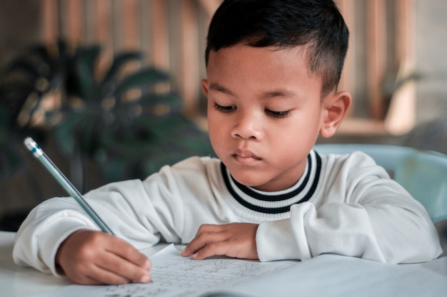 Enfant garçon tenant l'écriture au crayon. Garçon asiatique à faire ses devoirs, papier à lettres pour enfants, concept d'éducation, retour à l'école.