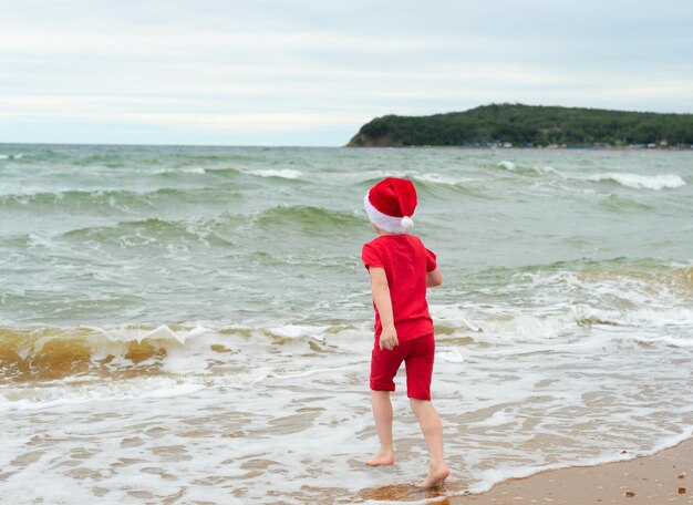 Enfant garçon en tissu rouge et chapeau de père Noël profitant de Noël sur la plage pendant les vacances de voyage de Noël concept de célébration de Noël ou du nouvel an