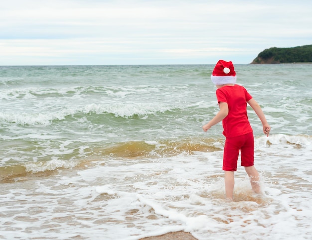 Enfant garçon en tissu rouge et chapeau de père Noël profitant de Noël sur la plage pendant les vacances de voyage de Noël concept de célébration de Noël ou du nouvel an