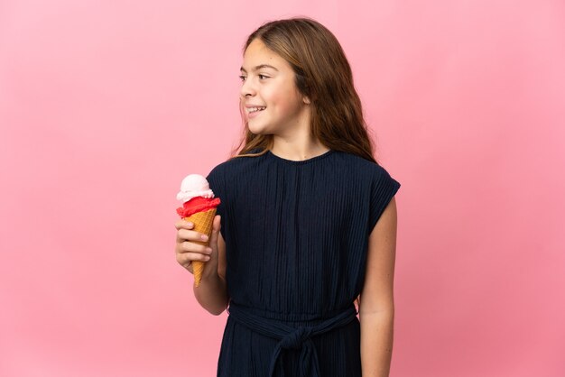 Enfant avec une glace au cornet sur fond rose isolé à côté