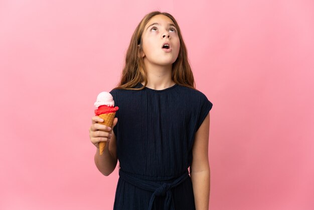 Enfant avec une glace au cornet sur fond rose isolé en levant et avec une expression surprise