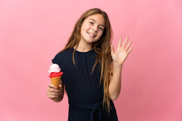 Enfant avec une glace cornet sur mur rose isolé saluant avec la main avec une expression heureuse
