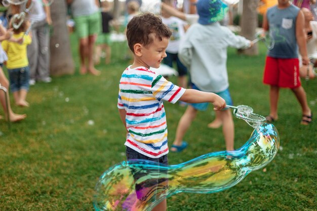 L'enfant gonfle de grandes bulles de savon programme d'animation de rue enfant heureux sur une pelouse verte d'été va