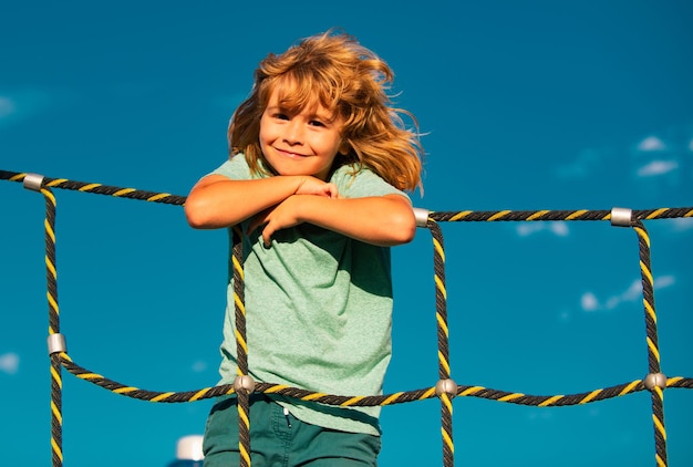 Enfant grimpant sur l'escalade dans le parc le jour d'été s'amusant en souriant à l'extérieur les enfants profitant de pla