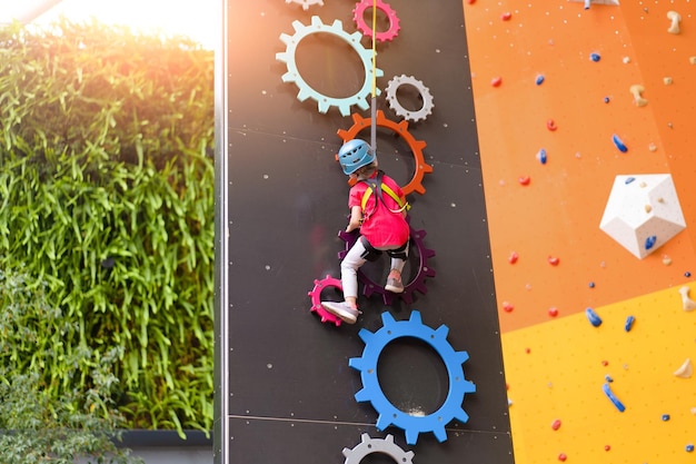 Enfant grimpant sur un mur dans un centre d'amusement Formation d'escalade pour enfants Petite fille en tenue d'escalade habillée grimper haut Loisirs actifs extrêmes pour les enfants