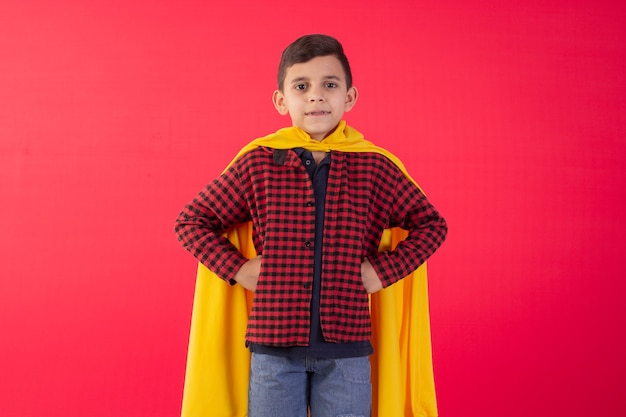 Enfant avec heeoi pose avec cape dans une photo de studio sur fond rouge.