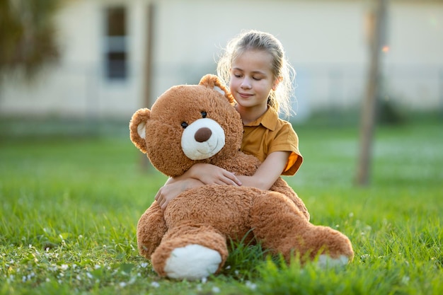 Une enfant heureuse étreignant son ami ours en peluche à l'extérieur sur la pelouse d'herbe verte Concept d'amitié