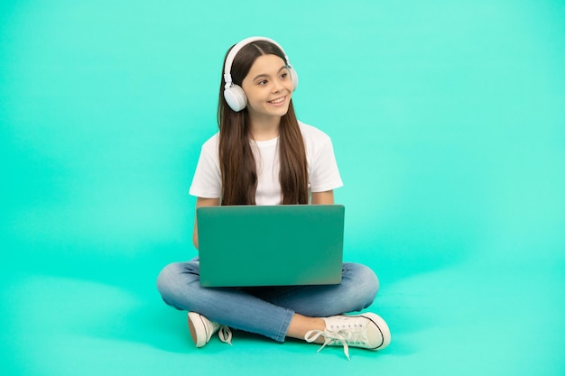 Une enfant heureuse utilise un ordinateur portable sans fil pour un appel vidéo ou écoute un webinaire dans un casque pour retourner à l'école