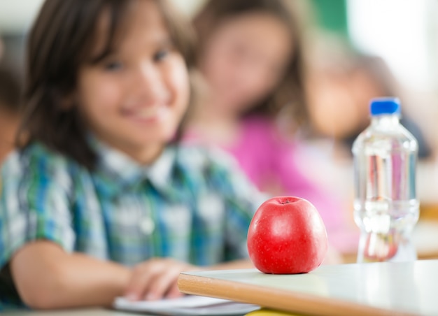 Photo enfant heureux avec apple et bouteille d'eau assis en classe et souriant