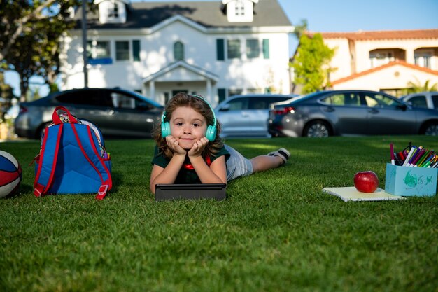 Un enfant heureux apprend en ligne dans une école virtuelle à l'aide d'une tablette sur l'herbe verte en plein air elearning