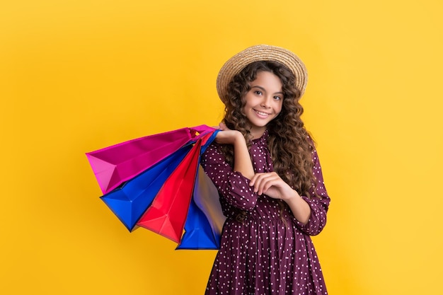 Un enfant heureux aux cheveux bouclés tient des sacs à provisions sur fond jaune