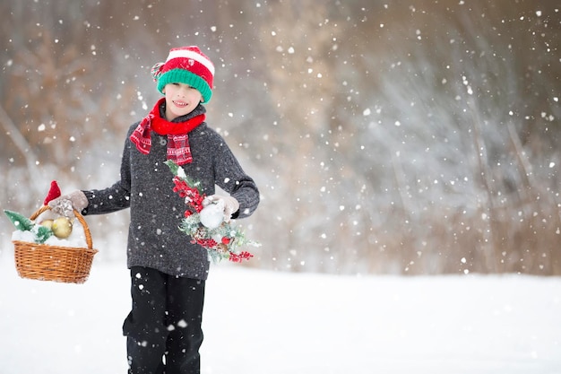 Un enfant heureux avant Noël avec des jouets de Noël se promène dans la forêt sous une chute de neige