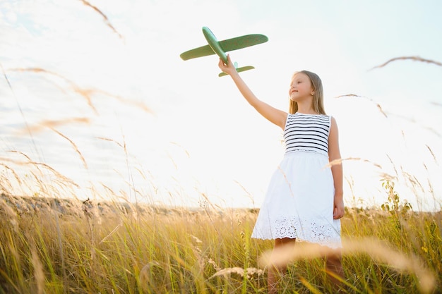 Un enfant heureux avec un avion jouet joue au coucher du soleil