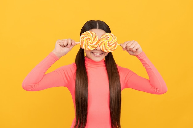 Enfant heureux avec des bonbons sucette sur bâton sur fond jaune, doux.