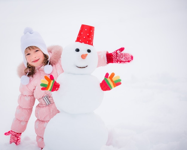 Enfant heureux et bonhomme de neige dans le parc d'hiver