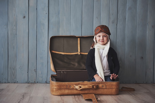 Enfant heureux en chapeau de pilote jouant avec une vieille valise. Enfance. Fantaisie, imagination. Vacances