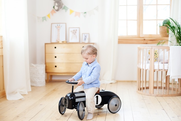 Enfant Heureux Conduit Une Voiture Vintage Jouet Dans Une Chambre D'enfant. Enfant Drôle Jouant à La Maison. Petit Garçon Actif Au Volant D'une Voiture Pour Enfants à La Maternelle. Tout-petit Au Volant D'une Voiture Rétro, Garçon Dans Une Petite Voiture