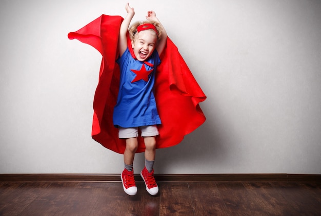 Enfant heureux en costume de super-héros contre le mur gris.