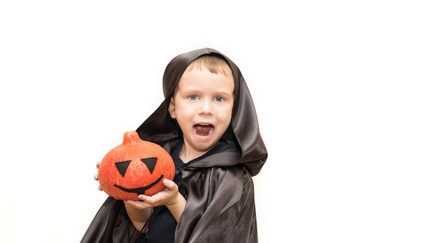 Enfant heureux dans un imperméable et une capuche avec une citrouille sur fond blanc Copiez le spase Le concept d'Halloween