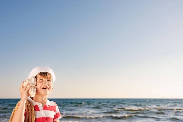 Un enfant heureux écoute un coquillage sur la plage