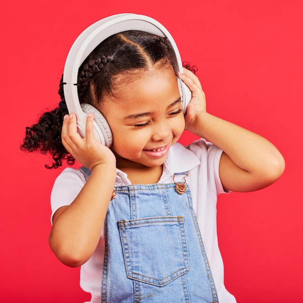 Photo enfant heureux et écouteurs pour radio musicale et podcast amusant sur fond rouge isolé et studio de danse souriez petite fille et enfant écoutant de la chanson audio de danse et des médias en streaming sur fond